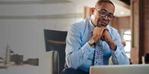 Man resting his head on his hands while looking at his laptop