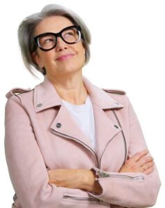 Older woman with gray hair wearing black glasses and a pale pink jacket, looking upward with arms crossed.