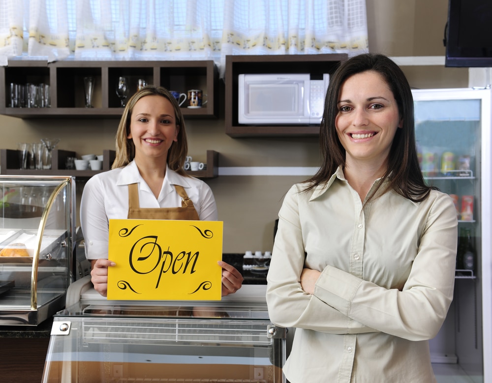 photo of two smiling women in a bakery holding a yellow open sign
