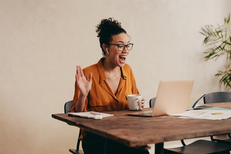 A smiling woman gets a virtual business coaching experience with The Entrepreneur’s Source on her home computer.