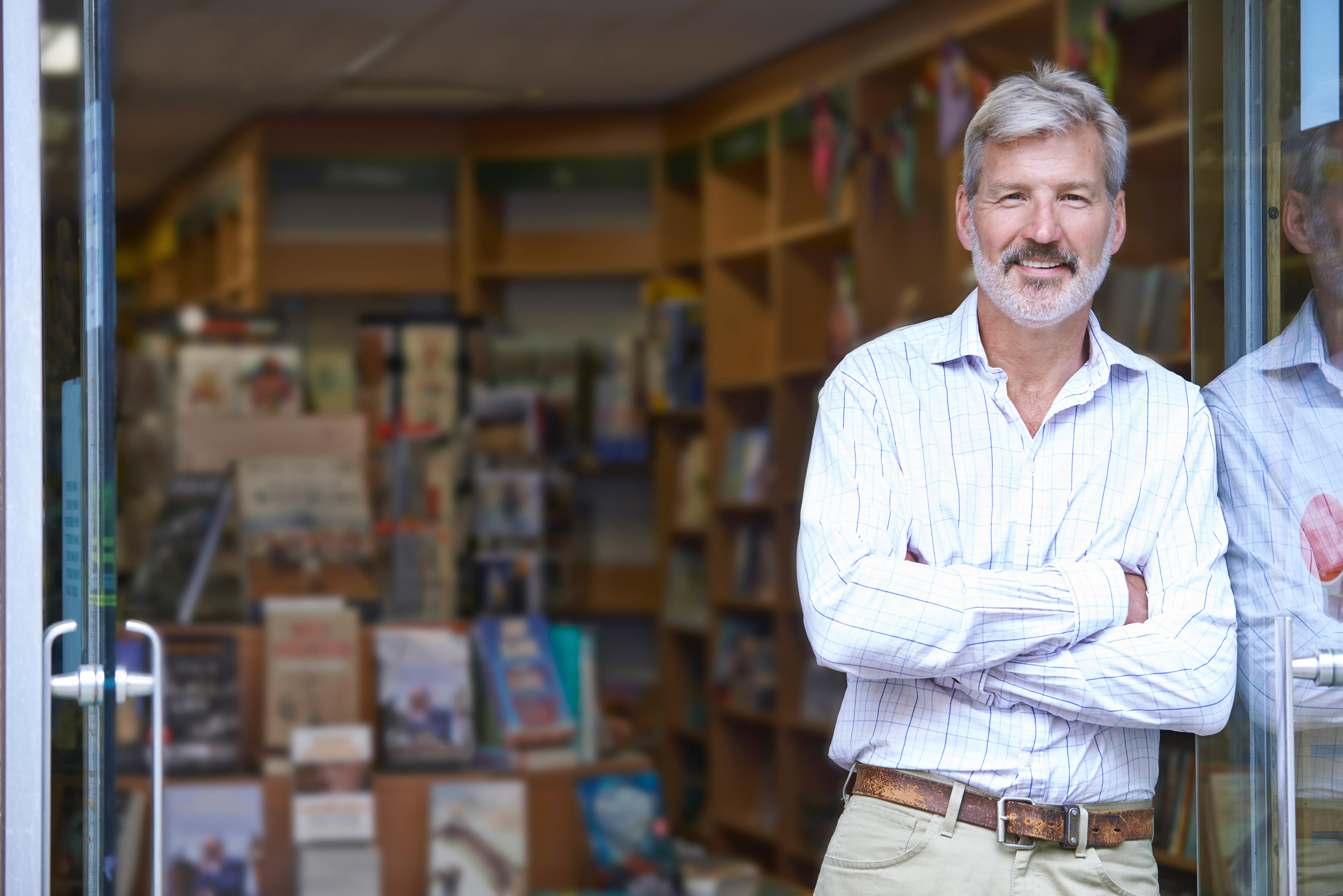 After working with an Entrepreneur’s Source Career Ownership Coach, an independent business owner smiles in the doorway of his bookstore.