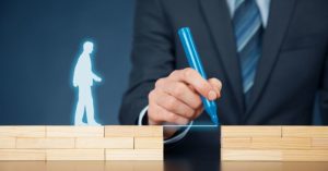 Man in a suit making a bridge with a pen between two wooden blocks for a man's silhouette to walk across.