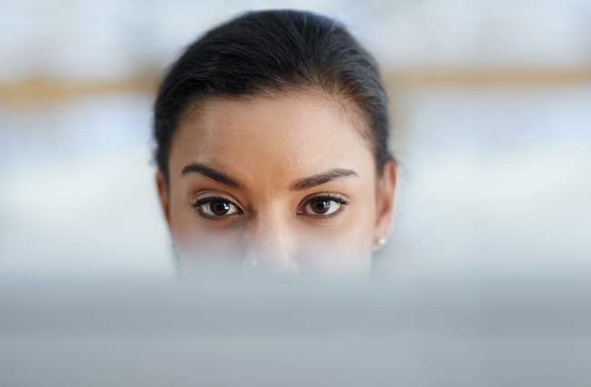 Close-up of a woman's eyes peeking over a blurred surface, looking ahead curiously.