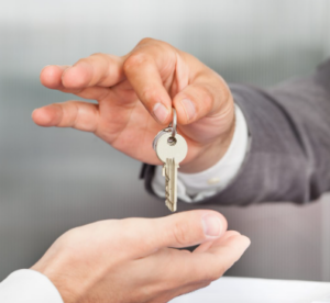Two hands exchange a metal key, symbolizing handing over possession or access.