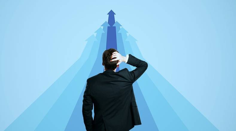 Man in a suit facing upward blue arrows converging to a peak, symbolizing career growth and goal pursuit.