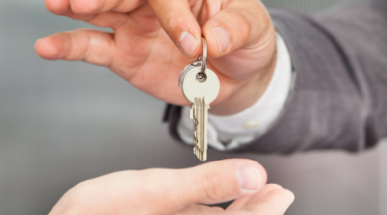 Two hands exchange a set of keys on a keyring, with the key being handed over to the other person