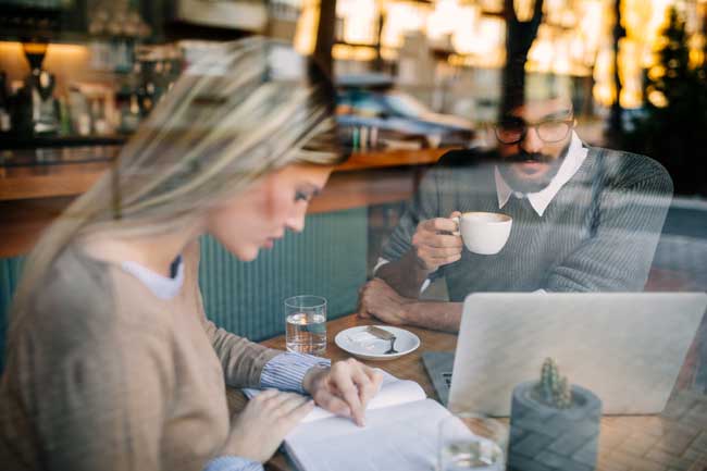 woman-reading-while-man-drinks-coffee-near-laptop